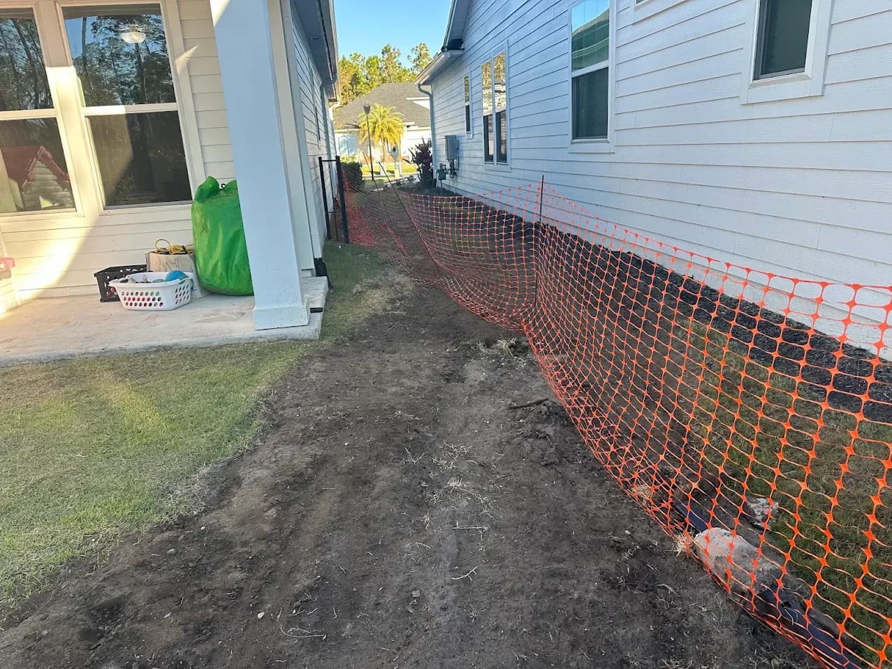 A Nocatee side yard along the property line with the grass stripped to bare dirt and orange construction safety fencing in place.