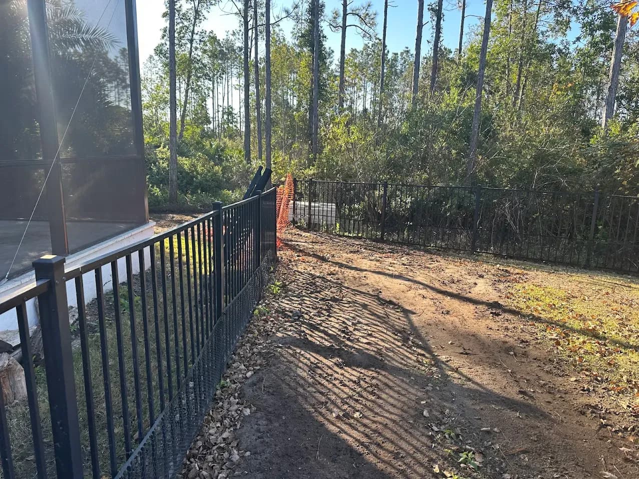 An aluminum fence with tire ruts and torn-up ground in the grass running alongside it.