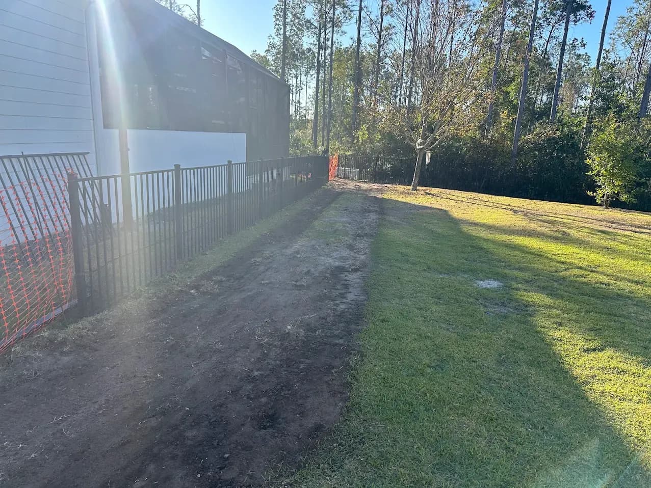 A bare strip of dirt where the lawn was, running along the side yard and screen enclosure.